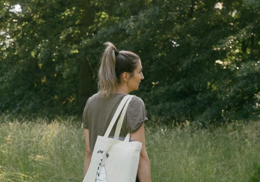 A woman walks in a meadow with a cloth bag with a picture of Moomintroll.