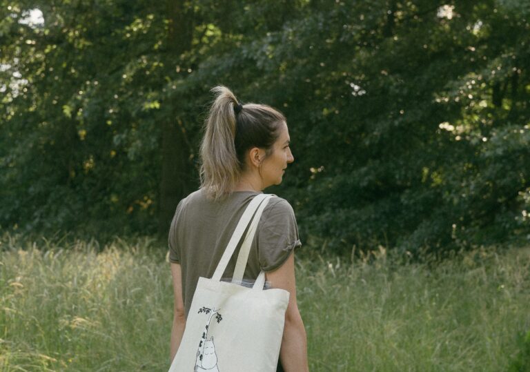 A woman walks in a meadow with a cloth bag with a picture of Moomintroll.