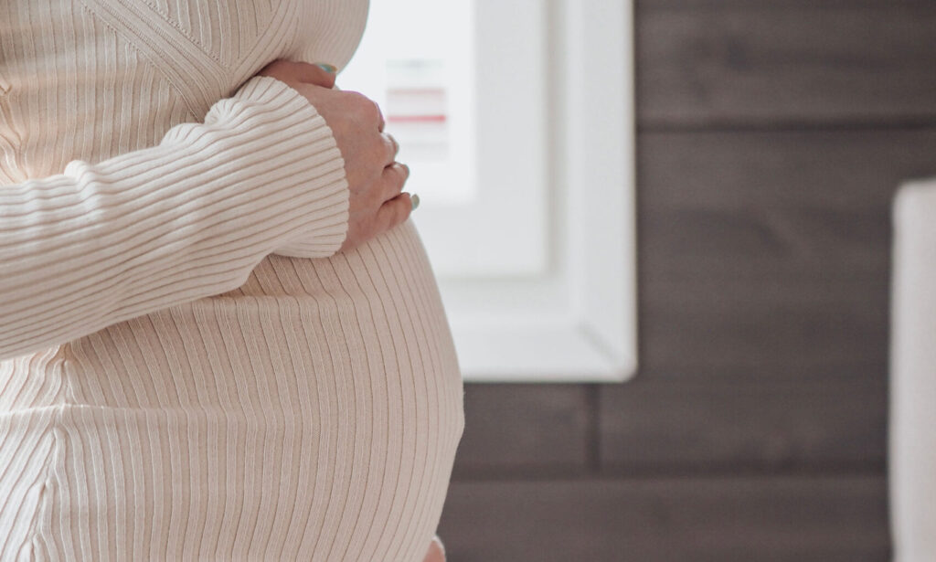 A pregnant woman holds her hands over her stomach.